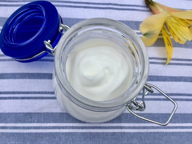 hand made body lotion in a glass jar with a yellow flower next to it