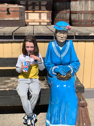 A girl sitting beside a statue of an old woman.