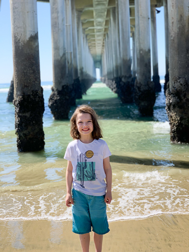 A girl standing on the sand in front of beach pillars.
