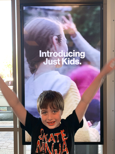boy standing in front of a verizon sign with arms up smiling