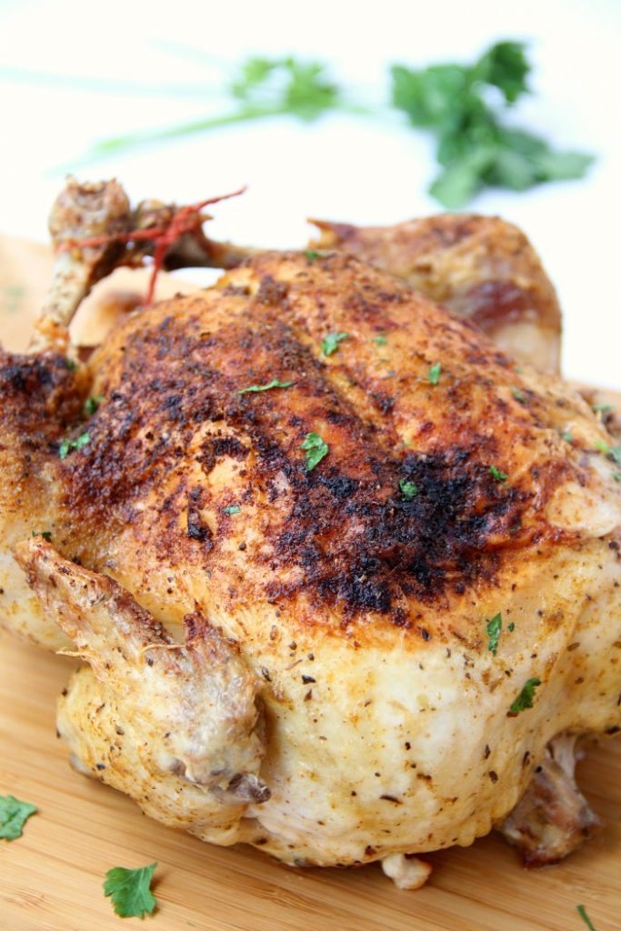 Photo of a roasted chicken close up on a wooden cutting board as part as a Ninja Foodi recipe. 