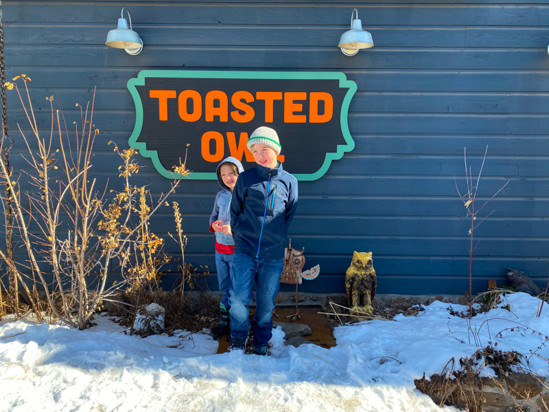 two boys standing outside in front of a sign saying Toasted Owl
