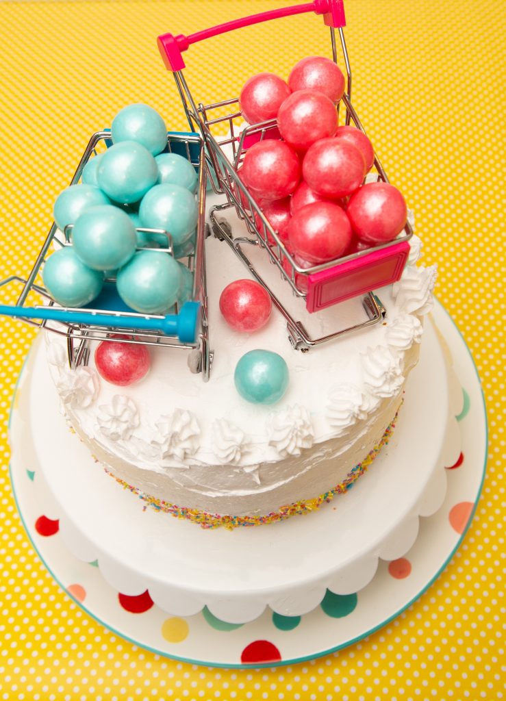 Gender reveal cake with gumballs in shopping carts on top