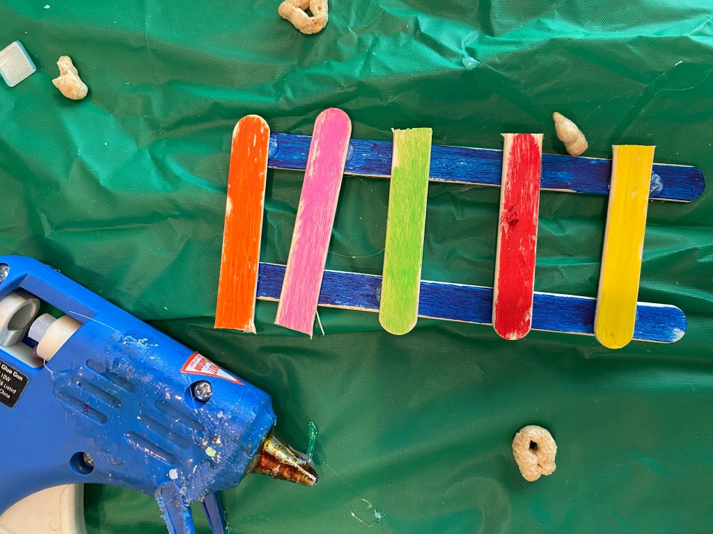 mini ladder made with popsicle sticks with a glue gun next to it for DIY Leprechaun Trap
